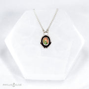 A super flashy Ethiopian Opal wrapped in a silver bezel is framed by a slim patinated shadowbox and hand carved details. Details: Solid sterling silver, partially recycled Ethiopian Opal Pendant: 10mm x 16mm 16” long Sterling Silver chain plus 2" extension Lobster-claw clasp